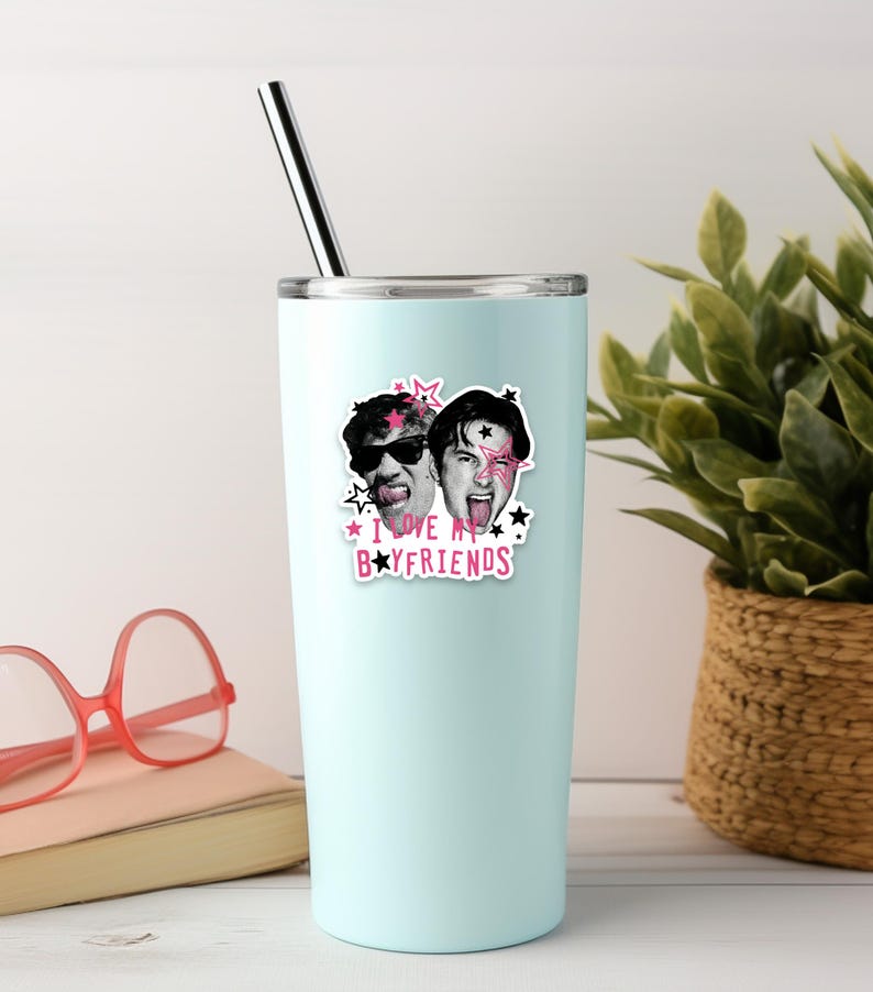 Op de afbeelding: Een lichtblauwe roestvrijstalen beker met een metalen rietje, voorzien van een sticker van twee gezichten met zonnebrillen en uitgestoken tongen, omringd door roze en zwarte sterren en de tekst I LOVE MY BOYFRIENDS in roze en zwarte letters.