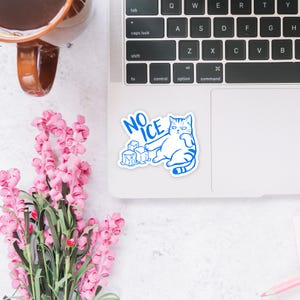 May include: A white sticker featuring a blue illustration of a cat with the text "NO ICE" and ice cubes. The cat is lying down with a grumpy expression. The sticker is on a laptop.