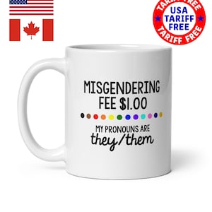 Könnte beinhalten: Weiße Keramik-Tasse mit dem Text "MISGENDERING FEE $1.00" und "MY PRONOUNS ARE they/them" in Schwarz. Unter dem Text befindet sich ein Regenbogen aus farbigen Punkten. Die Tasse hat einen weißen Henkel. Das Bild enthält auch die US-amerikanische und kanadische Flagge.