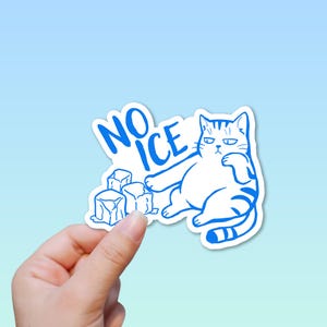 May include: A white sticker with a blue outline featuring a cartoon cat and the words "NO ICE". The cat is sitting with a grumpy expression next to several ice cubes. The sticker is held by a hand.