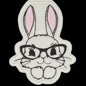 May include: White embroidered patch of a bunny wearing black-rimmed glasses. The bunny has pink ears and a white face.