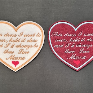May include: Two felt heart-shaped patches with embroidered text. The left patch is beige with gold embroidery and the right patch is burgundy with white embroidery. Both patches have the text "This dress I used to wear, hold it close and I'll always be there Love Mama" with a small red heart at the bottom.