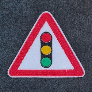 May include: Red, yellow, and green traffic light symbol on a white triangle with a red border. The symbol is a warning sign.