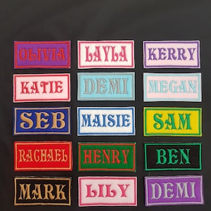 May include: A collection of 15 colourful iron-on name patches with various names, including Olivia, Layla, Kerry, Katie, Demi, Megan, Seb, Maisie, Sam, Rachael, Henry, Ben, Mark, Lily, and Demi.