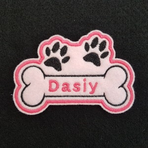 May include: Pink and black embroidered dog bone patch with the name "Dasiy" in pink lettering.