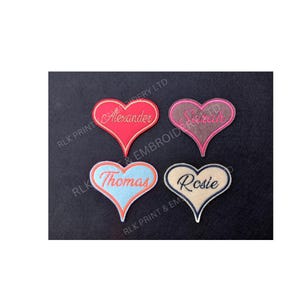 May include: Four heart-shaped embroidered patches, each bearing a name: "Alexander," "Sarah," "Thomas," and "Rosie." The patches feature various colour schemes, with the names stitched in contrasting colours. They are displayed against a dark backdrop.