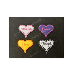 May include: Four heart-shaped embroidered patches, each with a name: Amelia Rose, Isaac, Eva, and Joseph. The patches are in pink, purple, yellow, and white. The names are in a cursive font. The patches are displayed on a black background.