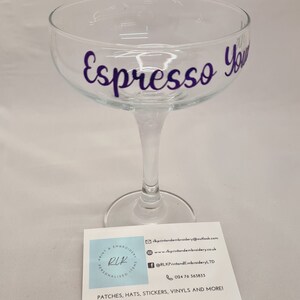 Puede incluir: Una copa de champ&aacute;n de cristal transparente con el texto "Espresso You" en letras moradas.
