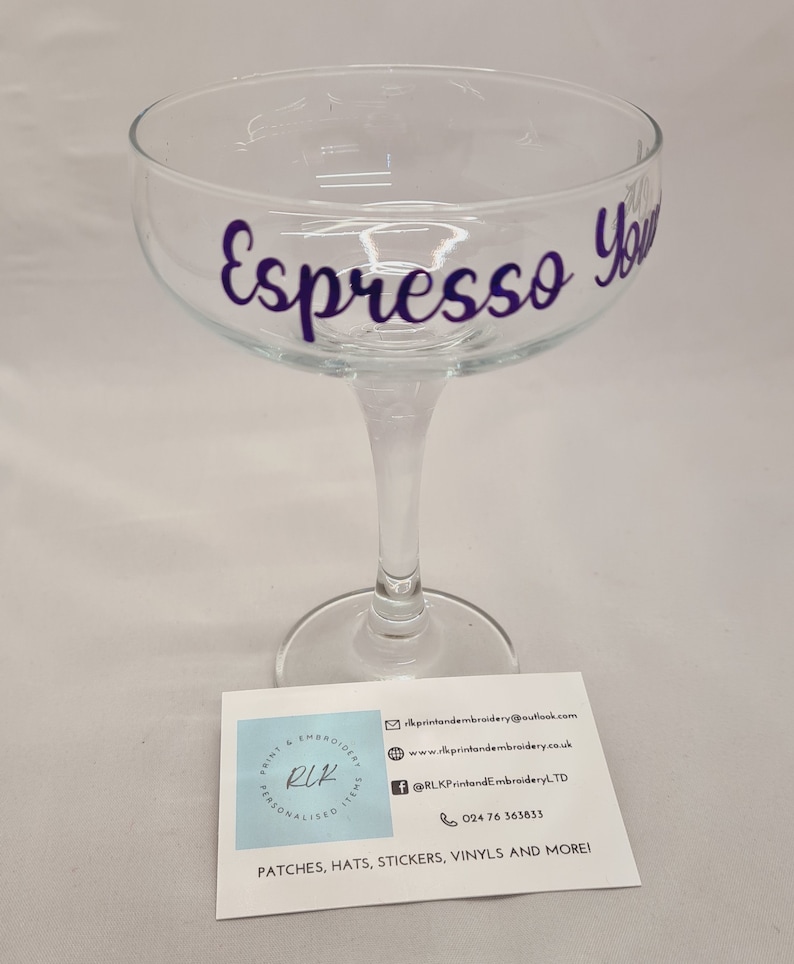 Puede incluir: Una copa de champ&aacute;n de cristal transparente con el texto "Espresso You" en letras moradas.