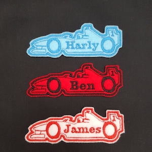 May include: Three embroidered iron-on patches shaped like racing cars. The top patch is light blue with the name "Harly" in black. The middle patch is red with the name "Ben" in black. The bottom patch is white with the name "James" in red.