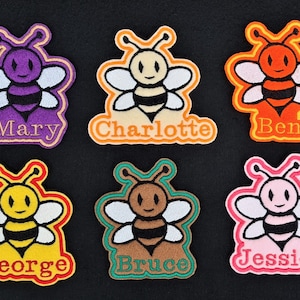 May include: Six colourful bee-shaped iron-on patches with different names: Mary, Charlotte, Ben, George, Bruce, and Jessica.