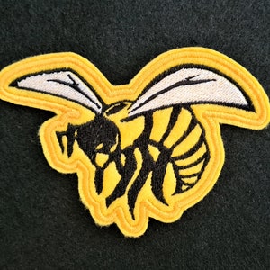 May include: Yellow embroidered patch of a black and white wasp with wings. The patch is outlined in yellow thread.
