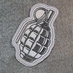 May include: A black and white embroidered patch of a grenade with a pull pin. The patch is surrounded by a grey outline.