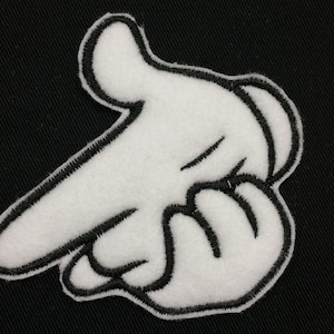 May include: White felt hand patch with black outline, pointing to the left. The hand is in a 'peace' sign gesture.