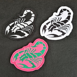 May include: Three embroidered iron-on patches featuring a scorpion design. The scorpions are black and white on a black background, black on a white background, and green on a pink background.