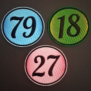 May include: Three embroidered patches with the numbers 79, 18, and 27. The patches are circular and have a textured background. The numbers are black and the backgrounds are blue, green, and pink.
