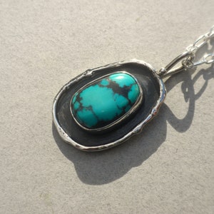 May include: A silver chain necklace with a turquoise stone pendant set in a silver frame. The frame has a rough, textured edge.