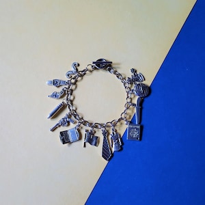 May include: A silver charm bracelet with various charms, including a watch, gun, bullet, flag, tie, passport, and globe. The bracelet is displayed on a yellow and blue background.