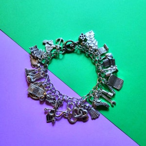 May include: A silver charm bracelet with a variety of charms, including a playing card, a ship, a money bill, a wrench, a heart, and a handcuff.