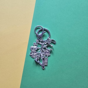 May include: A silver keychain with multiple charms, including a compass, a phone, a wrench, and a fire hydrant. The keychain is on a green and yellow background.
