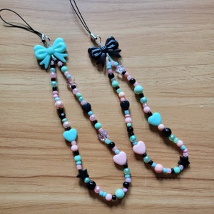 May include: Two phone charms with black bows and beads in pink, green, and black. The charms feature hearts and stars.