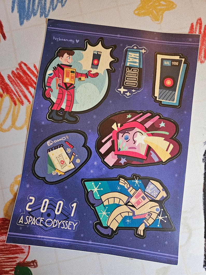 May include: A set of five stickers featuring characters and objects from the film "2001: A Space Odyssey". The stickers are on a blue background with stars. The stickers include a red space suit, a HAL 9000 computer, a red and white spaceship, a notepad with a pencil, and a spaceman floating in space.