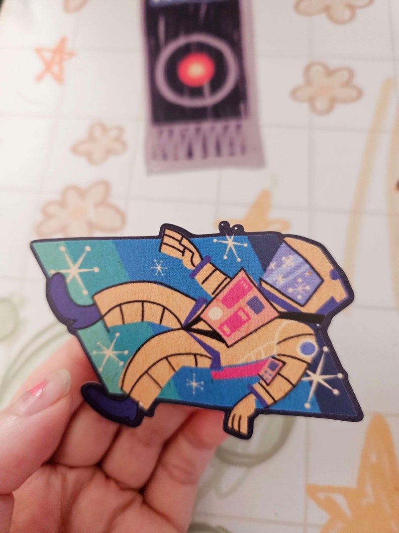 May include: A yellow astronaut sticker with a blue, green, and yellow space background. The astronaut is wearing a helmet and has a pink and blue space suit. The sticker has a retro, 1950s style.