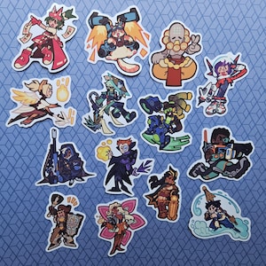 Op de afbeelding: Een verzameling van veertien kleurrijke, gestanste stickers met gestileerde stripfiguren in dynamische houdingen. De ontwerpen bevatten diverse figuren met opvallende outfits, wapens en accessoires, weergegeven in een levendige, krachtige tekenstijl.