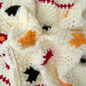 May include: A crocheted blanket with a white background and colorful squares. The squares are made with different colored yarns, including red, orange, yellow, green, and black.