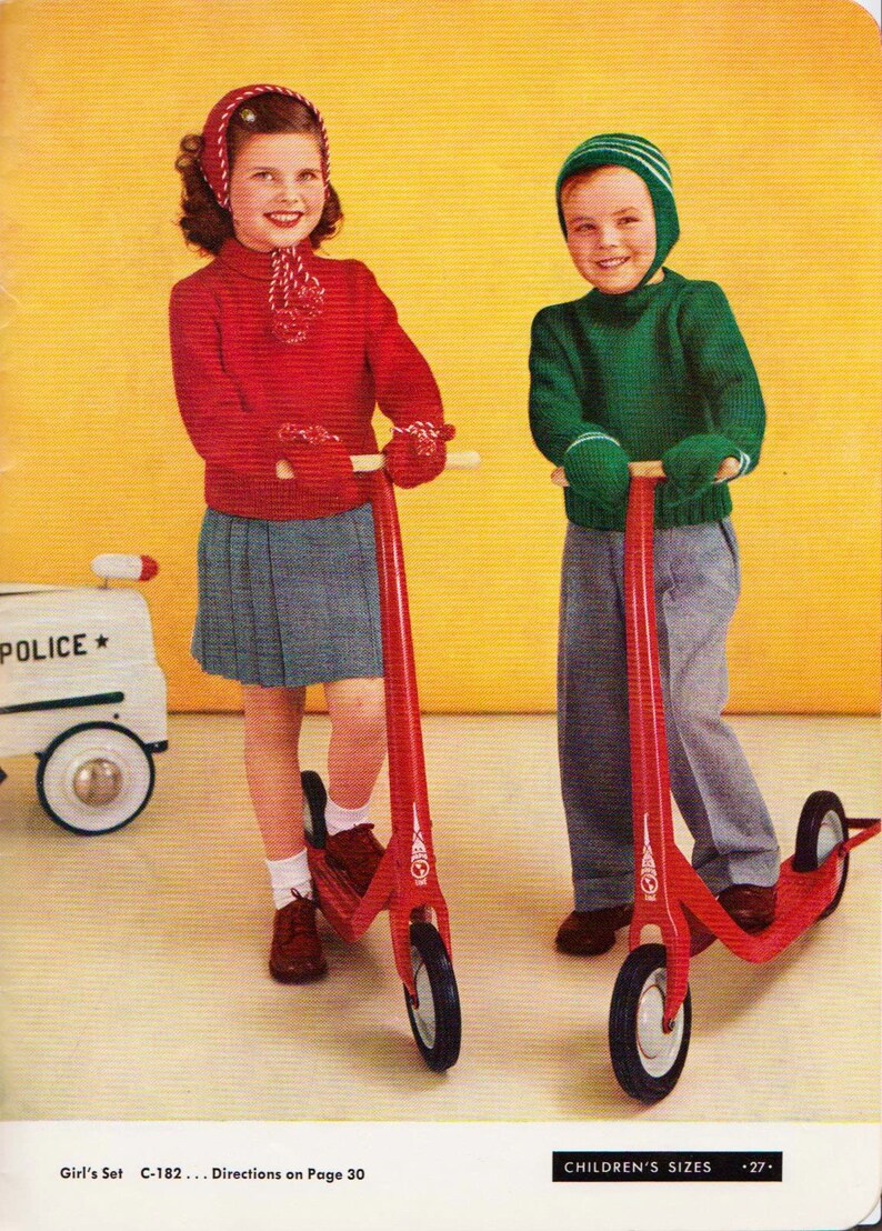 May include: Two children, a girl and a boy, are riding red scooters. The girl is wearing a red sweater, a red and white hat, and a gray skirt. The boy is wearing a green sweater and a green and white hat. Both scooters have red handlebars and wheels.