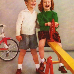 May include: Two children, a boy and a girl, are playing on a seesaw. The boy is wearing a white sweater and grey shorts. The girl is wearing a green sweater and a red and black plaid skirt. The seesaw is yellow and red.