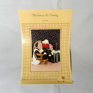 May include: A sewing pattern for a 18-inch Santa doll, titled "Christmas Is Coming" by "Farmyard Creations". The pattern shows a Santa doll sitting in a rocking chair with a candle and a book.