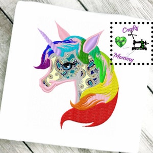 May include: Embroidered design of a rainbow unicorn head with a paisley pattern. The unicorn has a blue eye and a pink horn. The design is surrounded by a white background.