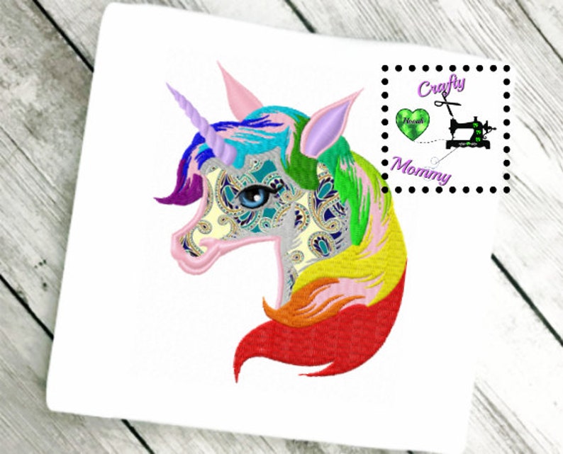 May include: Embroidered design of a rainbow unicorn head with a paisley pattern. The unicorn has a blue eye and a pink horn. The design is surrounded by a white background.