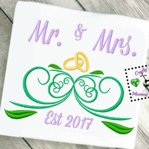 May include: Embroidered design featuring the words "Mr. & Mrs." in purple, with two gold rings above a green leafy design. The text "Est 2017" is also embroidered in purple below the design.