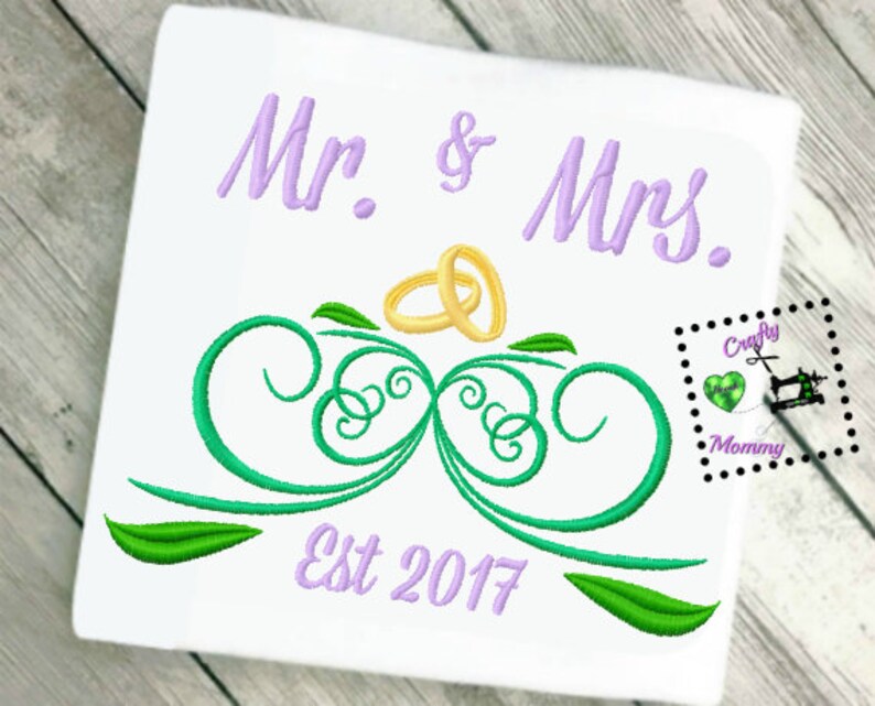 May include: Embroidered design featuring the words "Mr. & Mrs." in purple, with two gold rings above a green leafy design. The text "Est 2017" is also embroidered in purple below the design.