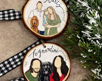May include: Two round wooden ornaments with painted portraits of families and their pets. The top ornament features a family of three with a dog, and the bottom ornament features a family of two with a dog. Both ornaments have the text "The [family name] Family" written on them.