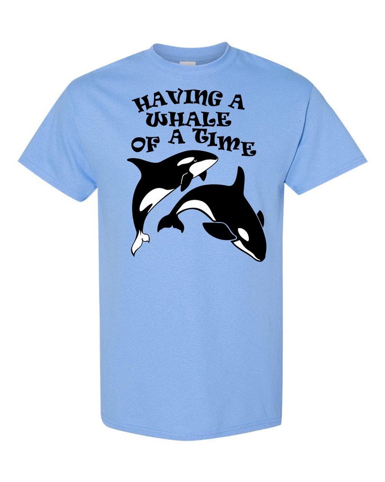 Puede incluir: Camiseta azul claro con un gr&aacute;fico negro de dos orcas y el texto "Having a Whale of a Time" en una fuente retro.