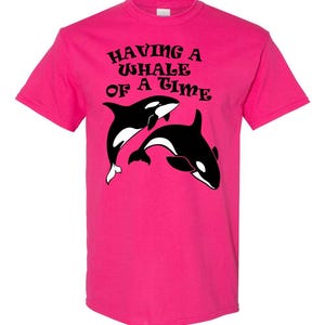 Puede incluir: Una camiseta rosa con un gr&aacute;fico negro de dos orcas y el texto "Having a Whale of a Time".