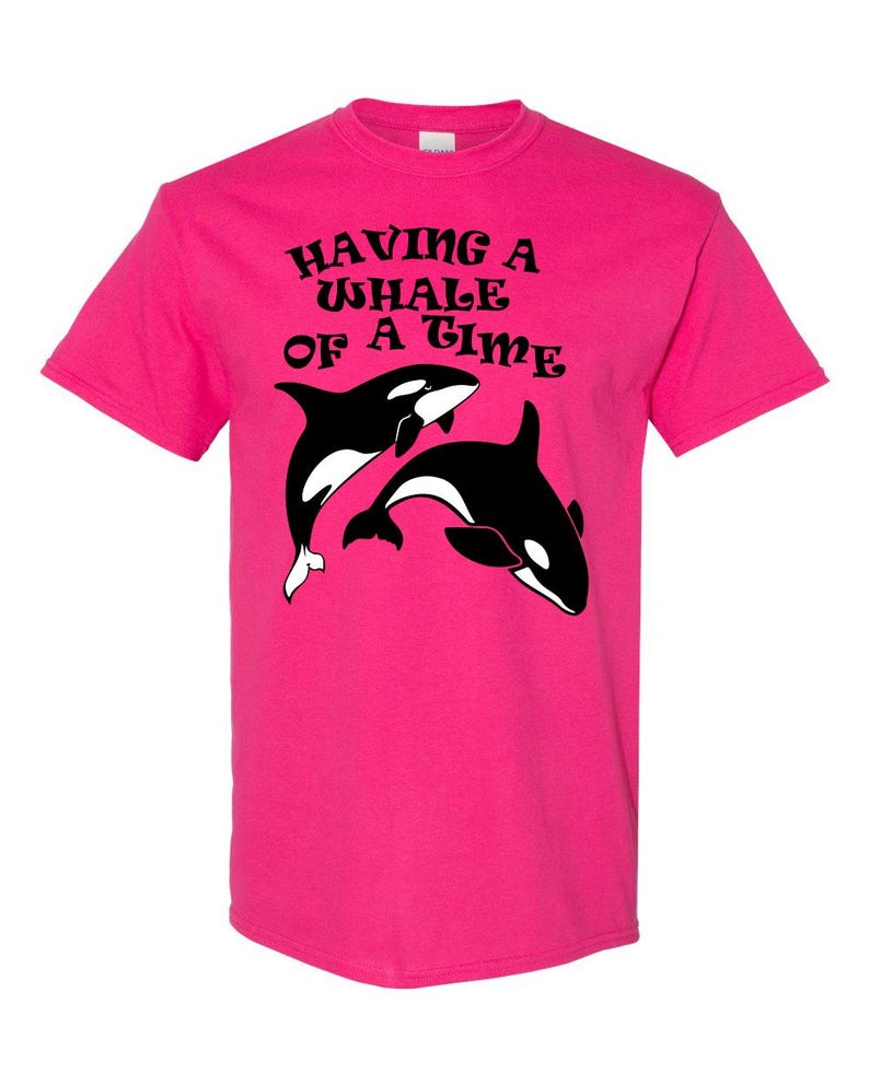 Puede incluir: Una camiseta rosa con un gr&aacute;fico negro de dos orcas y el texto "Having a Whale of a Time".