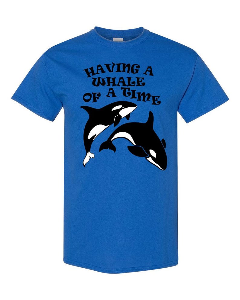 Puede incluir: Una camiseta azul real con un gr&aacute;fico en blanco y negro de dos orcas. El texto "HAVING A WHALE OF A TIME" est&aacute; impreso en negro en la camiseta.
