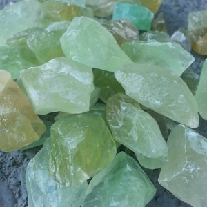 May include: A pile of light green and yellow crystal chips. The crystals are translucent and have a rough, natural texture.