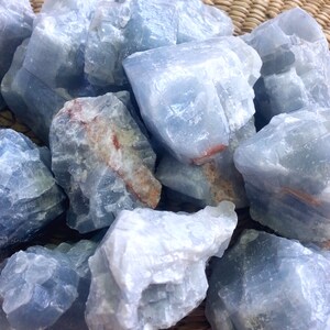 May include: A collection of blue calcite crystals, with a rough, natural texture. The crystals are various sizes and shapes, and have a light blue color with some white streaks.