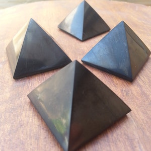 May include: Four black obsidian pyramids on a wooden surface. The pyramids are smooth and polished.