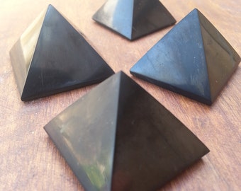 May include: Four black obsidian pyramids on a wooden surface. The pyramids are smooth and polished.