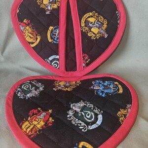 Peut inclure: Une paire de maniques matelassées en forme de cœur avec un fond noir orné des blasons colorés des quatre maisons de Poudlard. Les bords sont finis avec un biais en tissu rose vif et une petite boucle en tissu est fixée au centre supérieur.