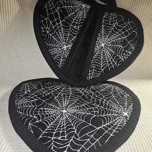 Könnte beinhalten: Ein Paar schwarze herzförmige Topflappen mit einem weißen Spinnennetz-Design.