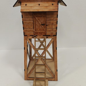 May include: A miniature wooden hunting blind or watchtower. The structure features a small cabin with a door, supported by a wooden frame and a ladder leading to the cabin. The wood has a natural, light brown color.