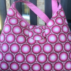 May include: A pink and white fabric tote bag with a circular pattern. The bag has two pink straps.