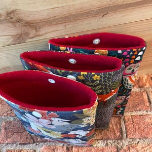 May include: Three fabric storage bags with floral, fox, and owl patterns. Each bag has a red interior and a snap closure. The bags are different sizes and are nested together.